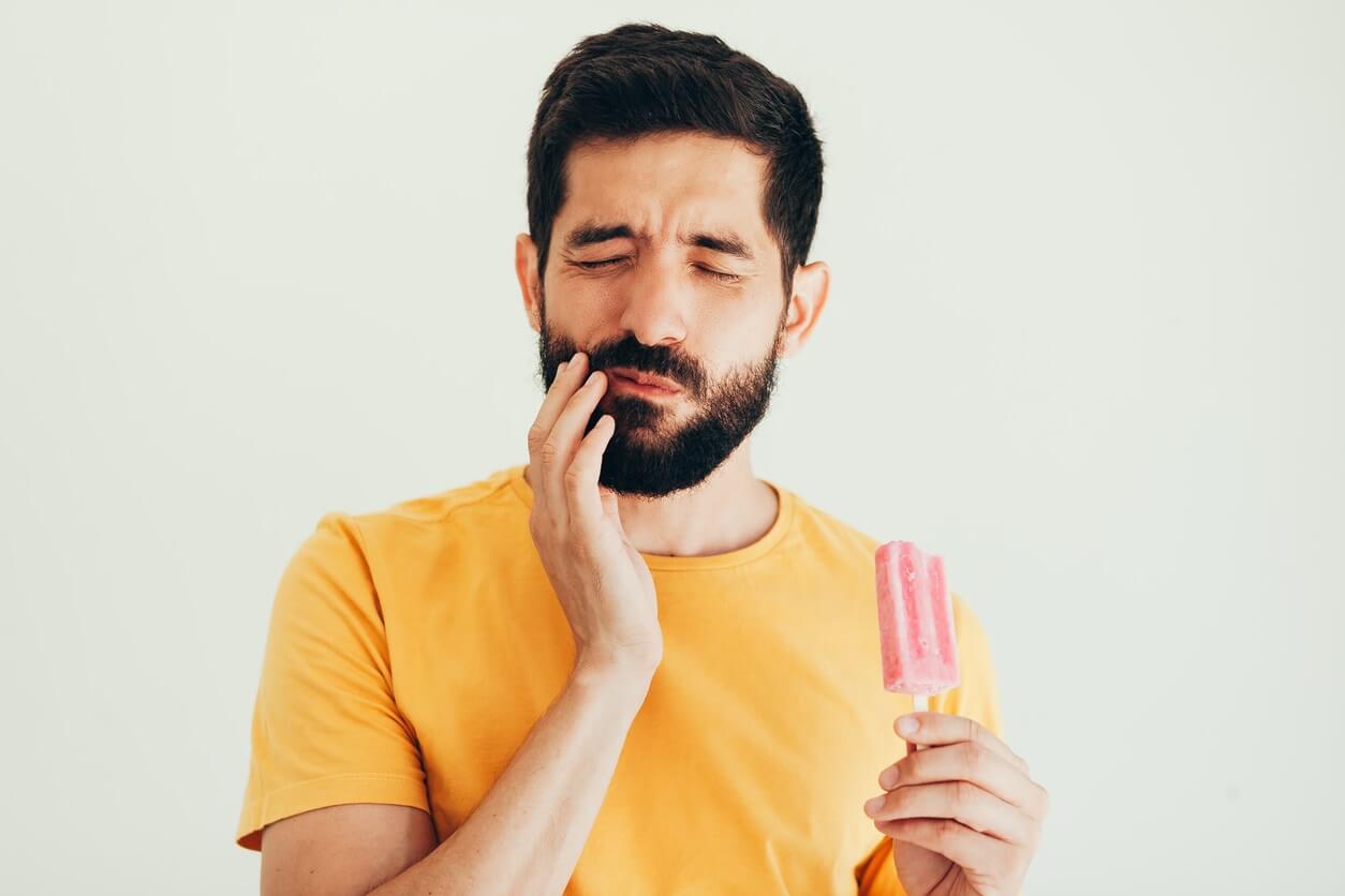 Stock image showing a male model feeling tooth sensitivity while eating an ice pop