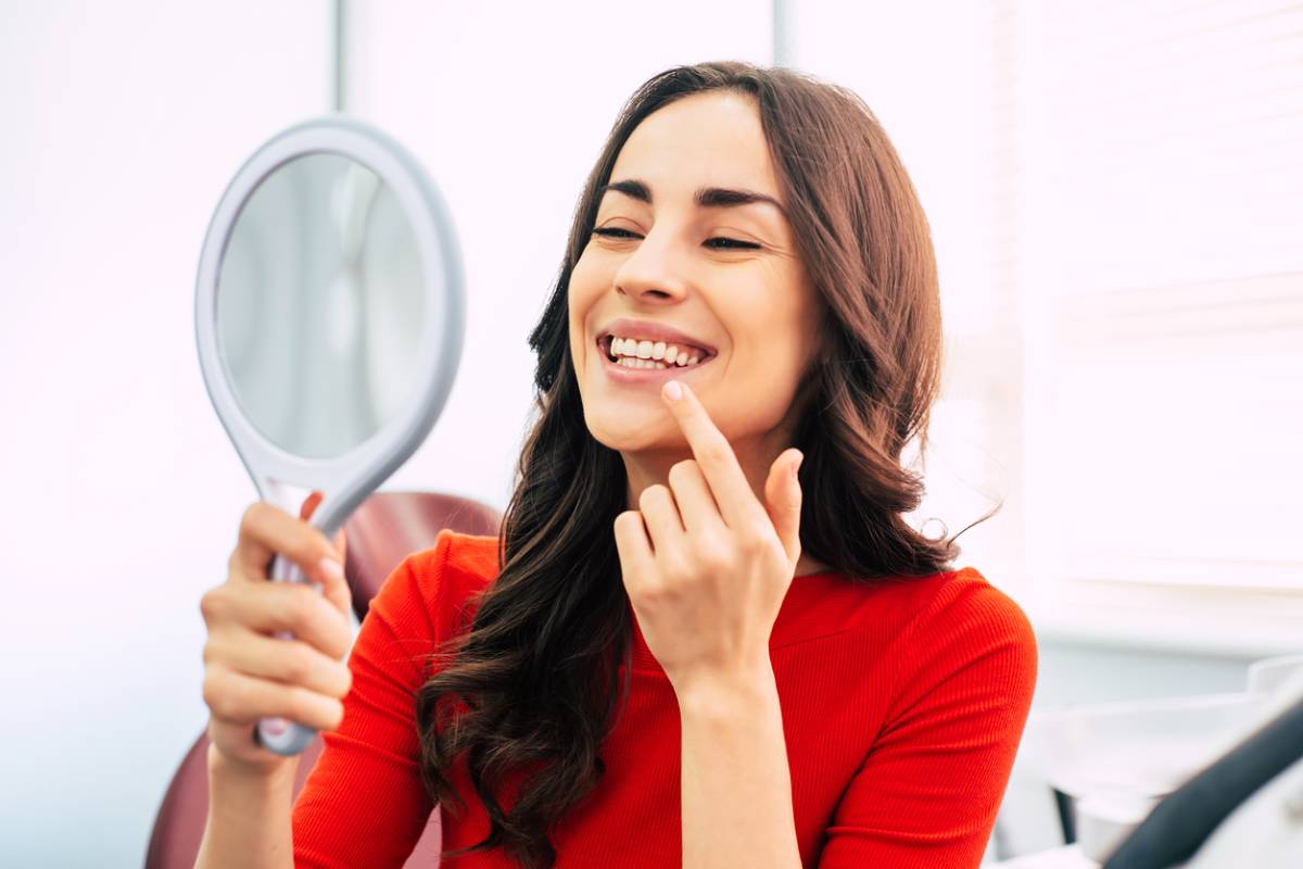 Stock image showing female model checking her smiling teeth holding mirror